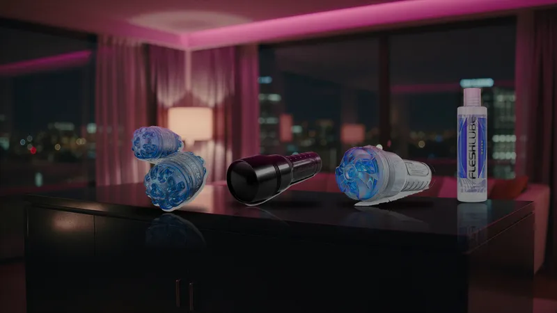 Quickshot Turbo, a closed black Fleshlight case, a Turbo Thrust sleeve, and Fleshlube Water in a row on a dark hotel dresser under pink neon