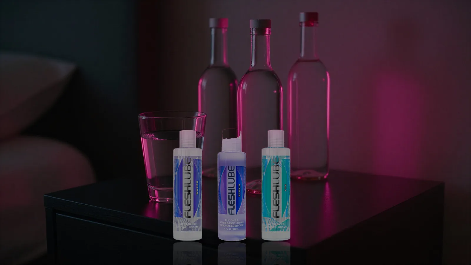 Three Fleshlube bottles — Water, Hybrid, and Ice — on a nightstand next to a glass of water